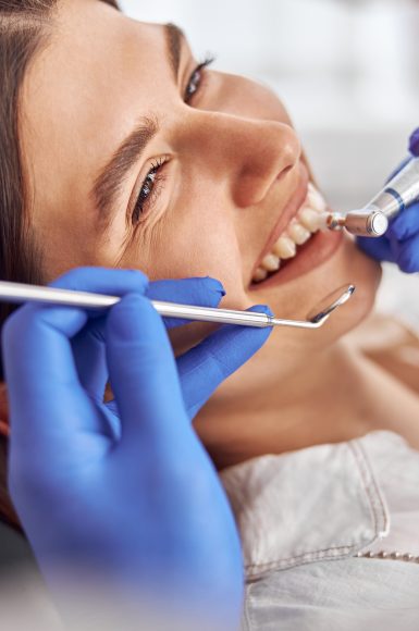 Female patient at dental procedure, doctor using dental instruments in modern dental clinic.
